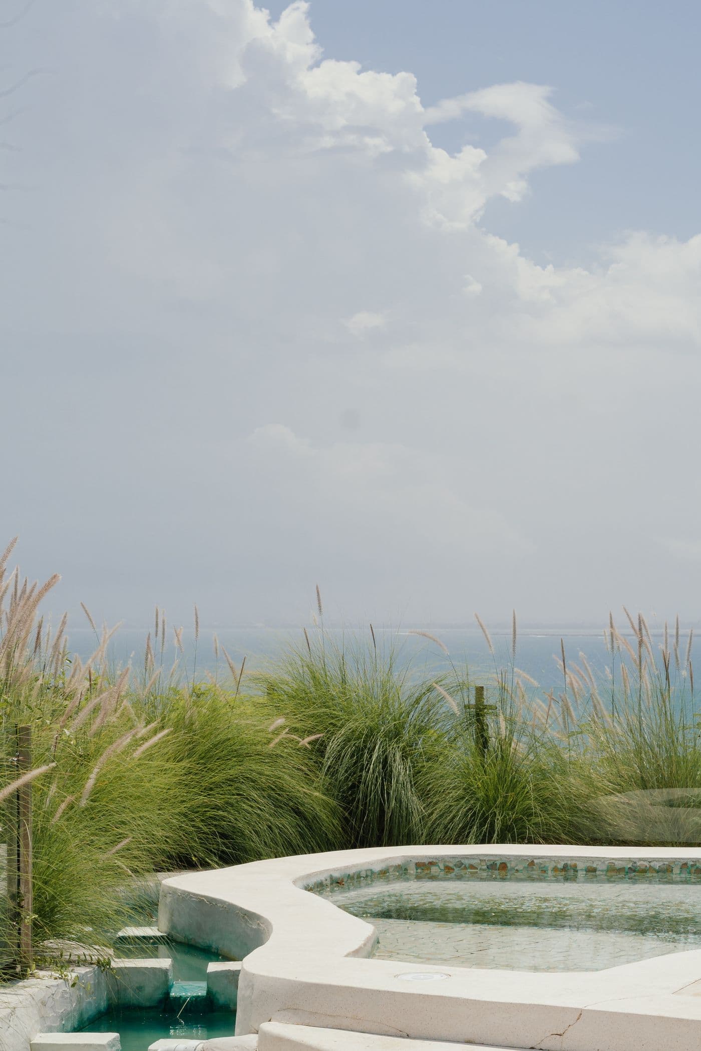 A white stone pool amid sea grasses above a hazy ocean